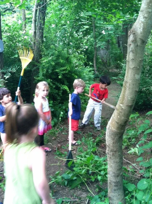Children helping rake and tend the wooded school grounds