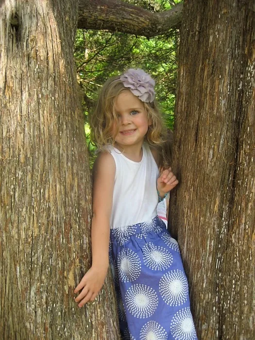 Girl peeking playfully through cedar trees